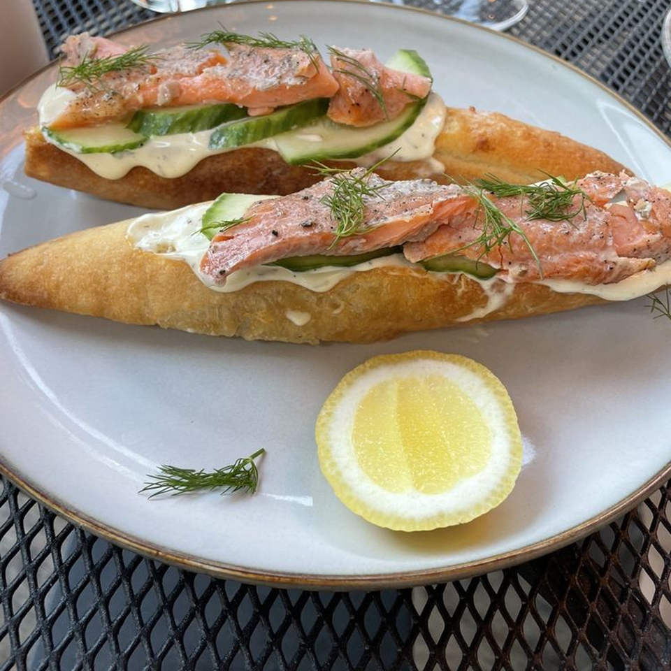 Two open-faced salmon sandwiches with cucumber, dill, and a lemon slice on a white plate.