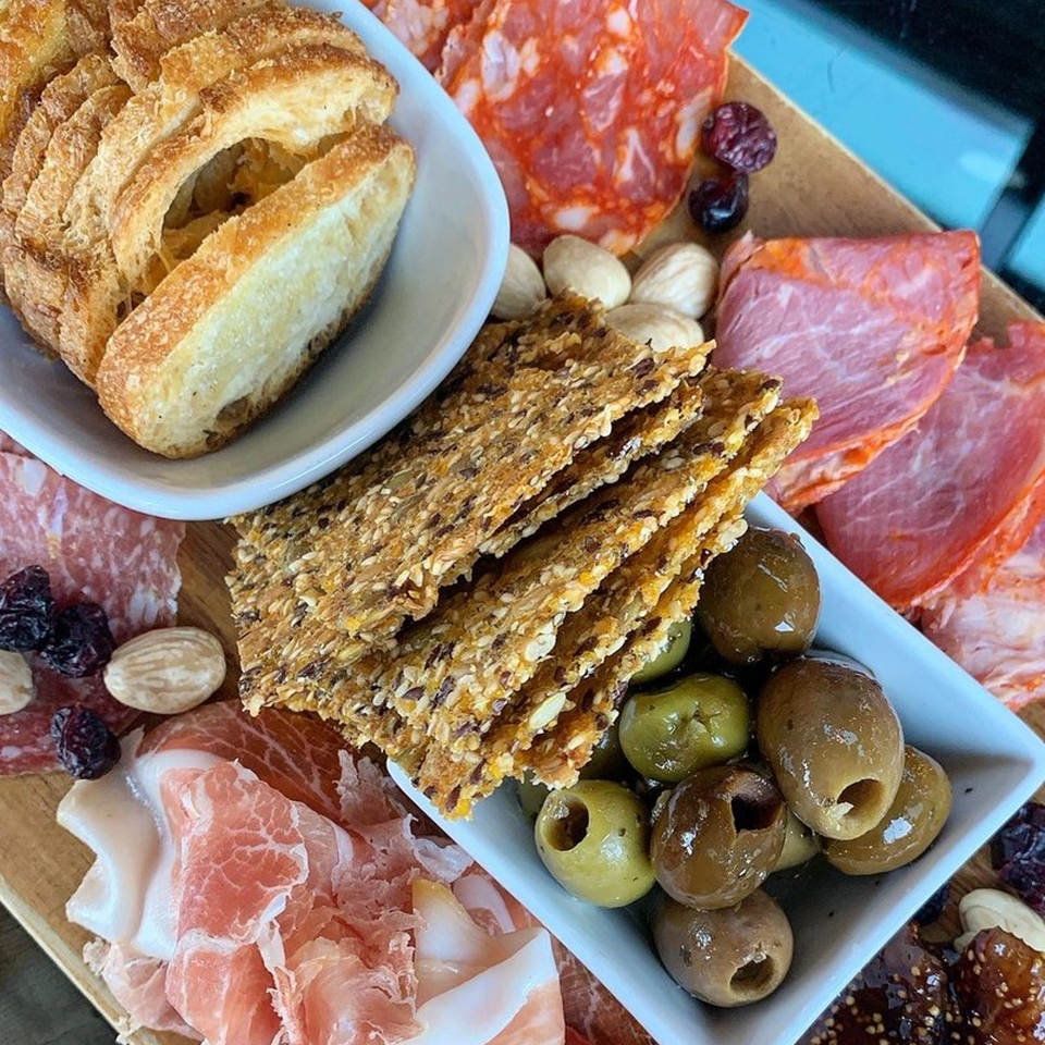 A charcuterie board with sliced meats, olives, crackers, bread, nuts, and dried fruit.