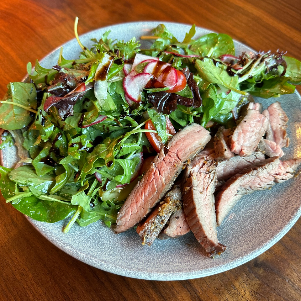 Sliced steak with a side salad of mixed greens, radishes, and cherry tomatoes, drizzled with balsamic.