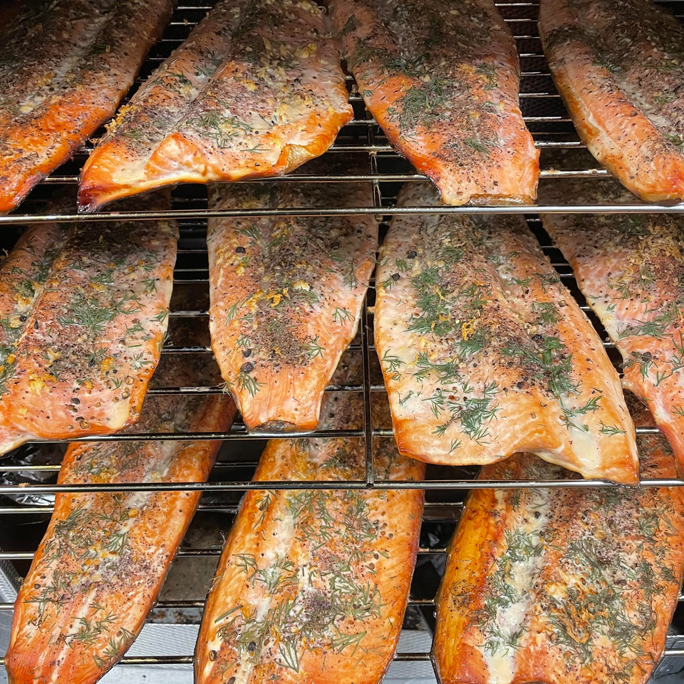 Multiple salmon fillets seasoned with dill and spices cooking on a grill rack.