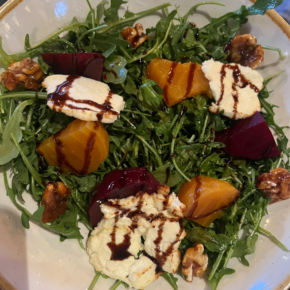 A vibrant beet and goat cheese salad with candied walnuts and balsamic glaze on a bed of arugula.